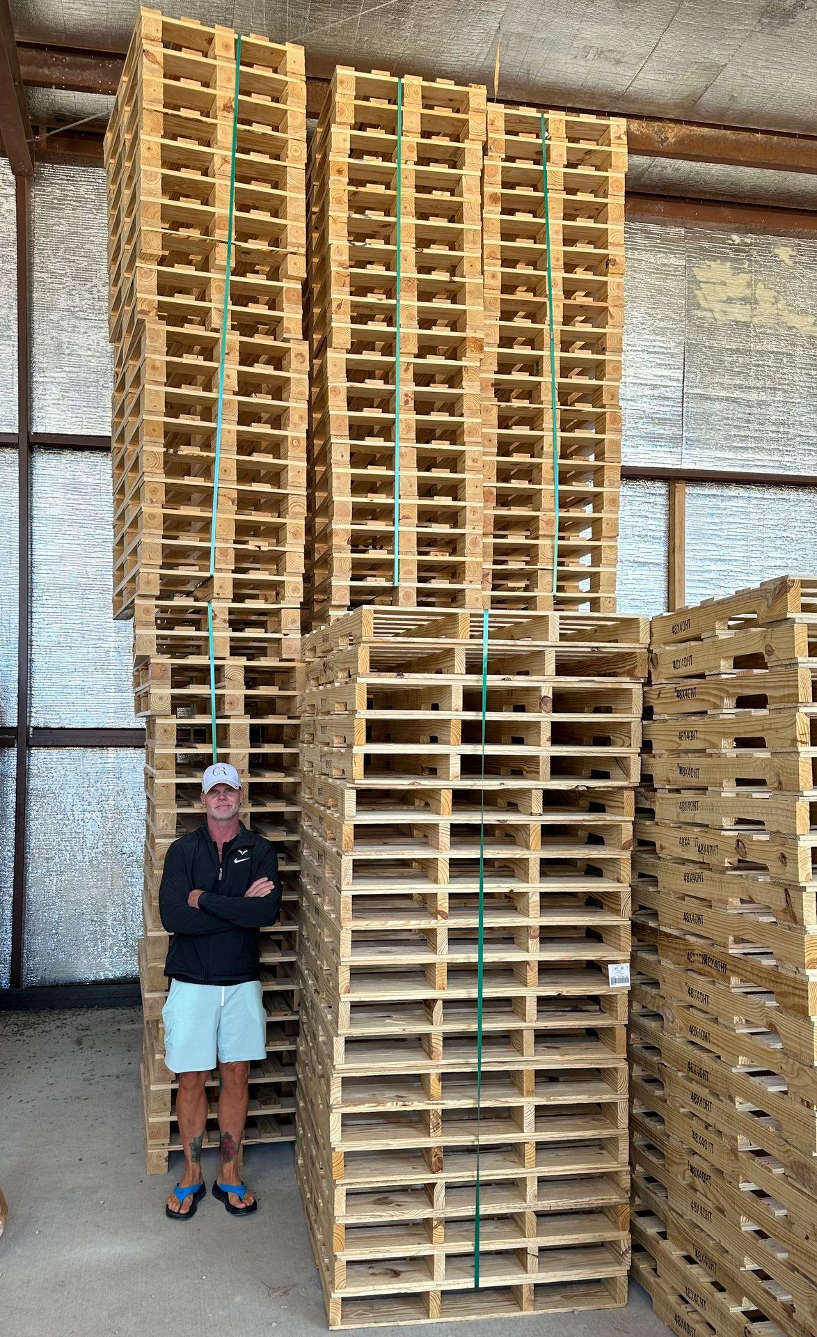 Several stacks of wooden pallets bound with green plastic straps inside an industrial warehouse with metal walls.