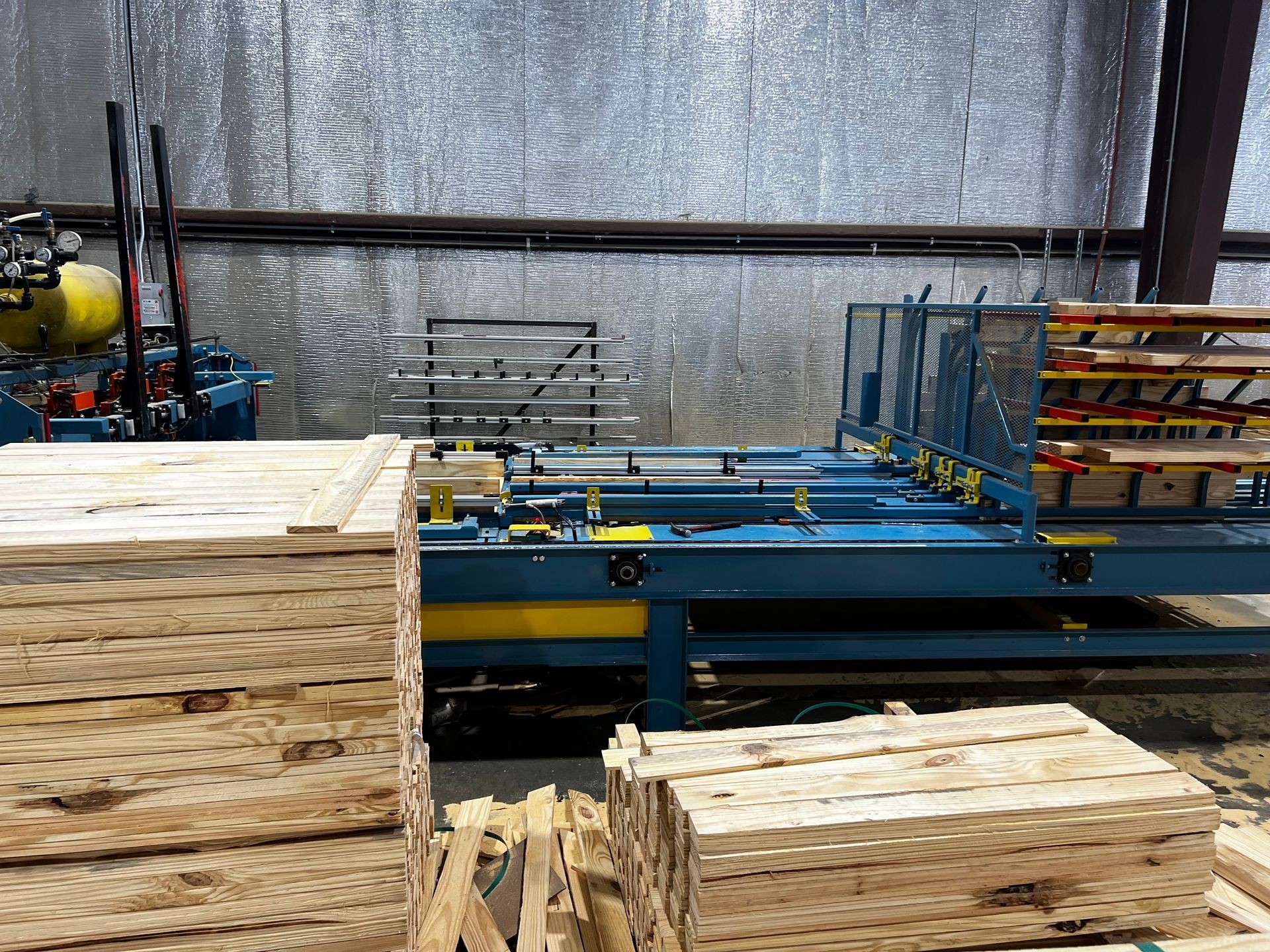 Industrial machine for processing and stacking wooden planks in a workshop with metal walls.