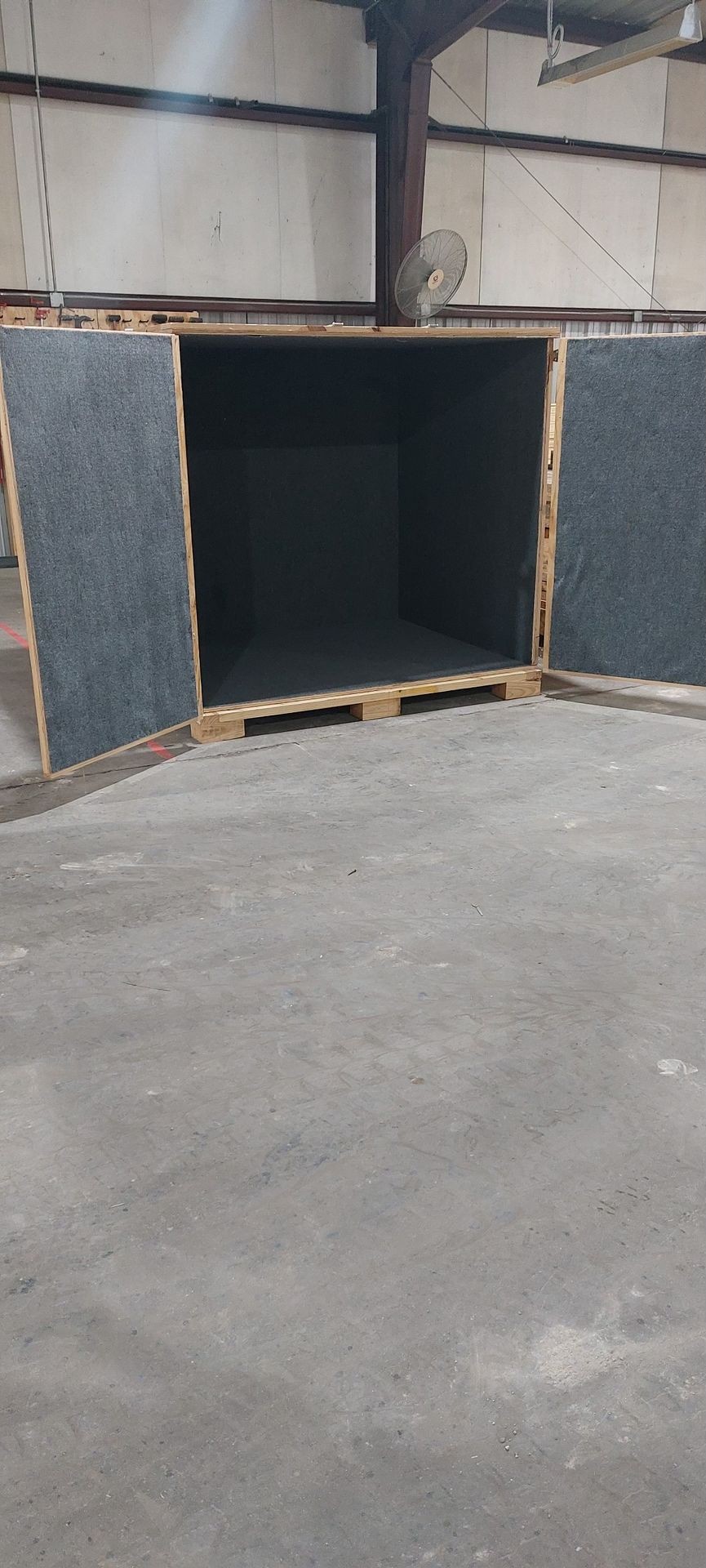 Large, open wooden box with fabric lining inside a spacious warehouse.